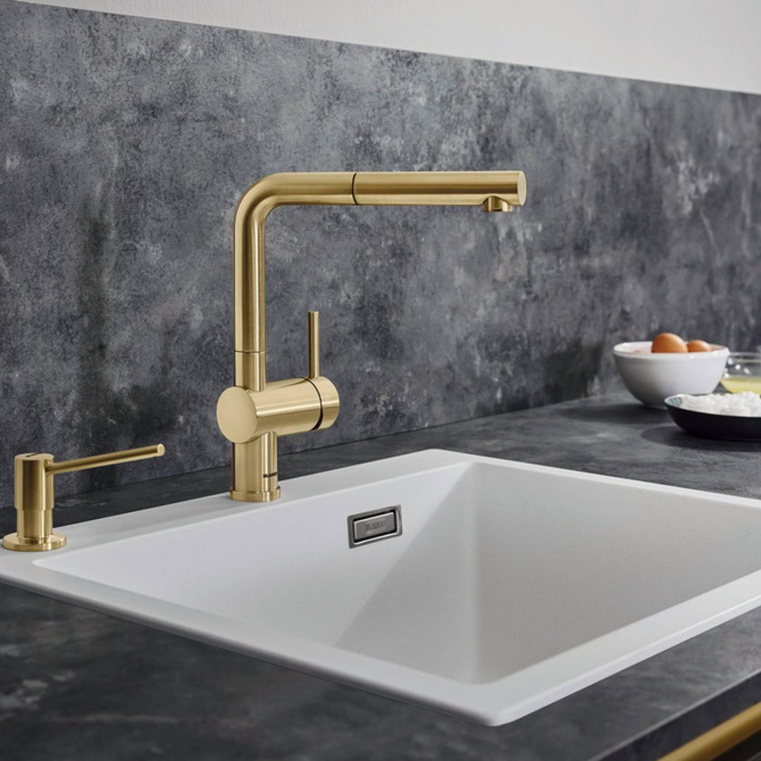 Satin gold tap and soap dispenser installed in a white sink with dark countertop