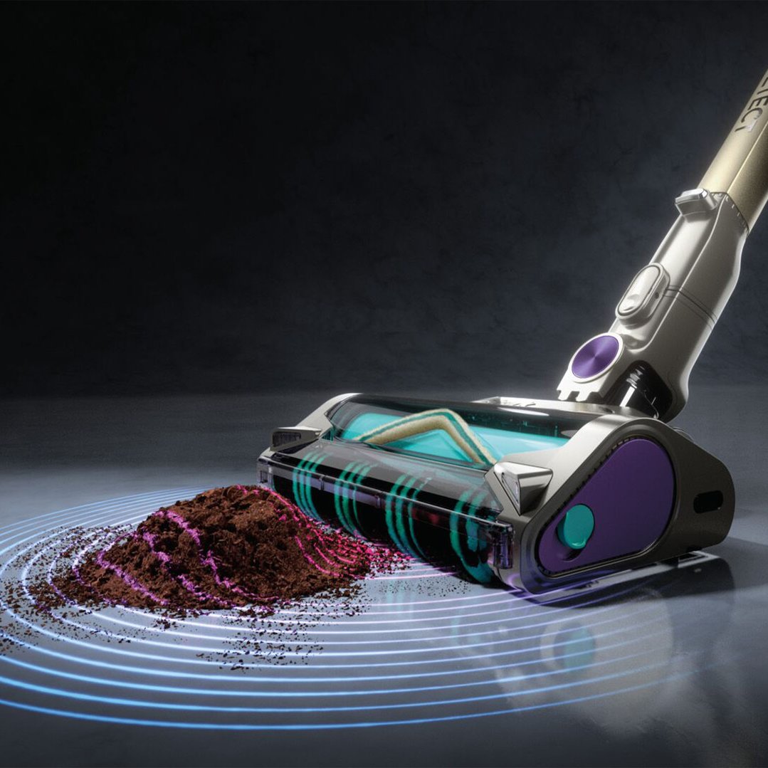 Cordless handstick vacuum cleaning a pile of dirt on a dark floor