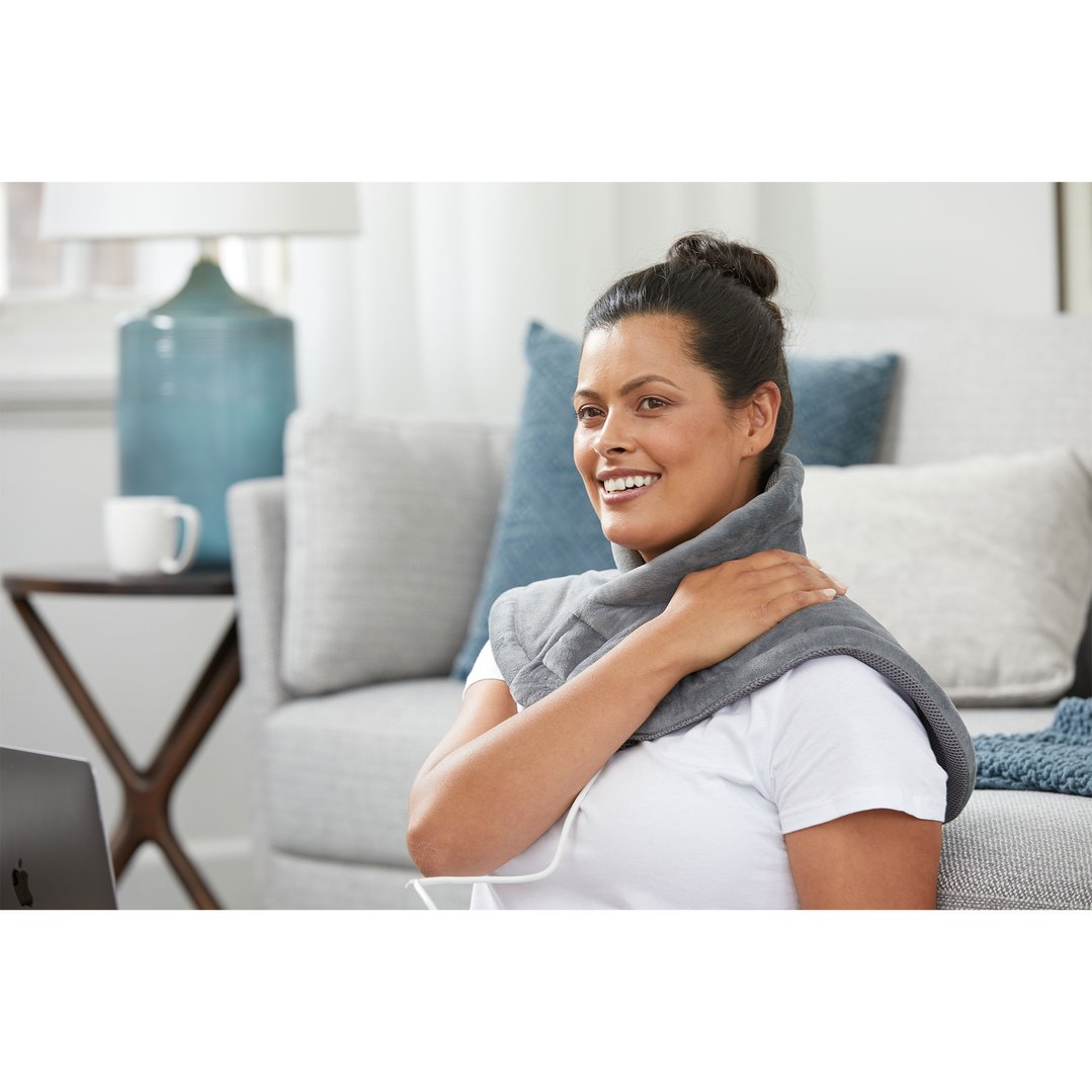 Woman wearing a grey electric blanket on her shoulders and neck in a living room