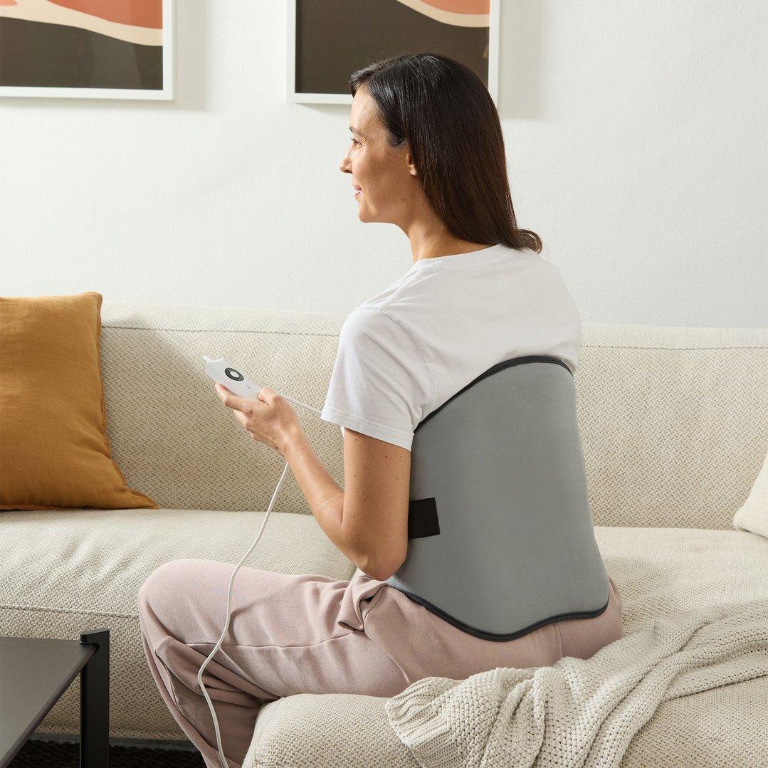 Woman sitting on a sofa using a heating pad for her lower back
