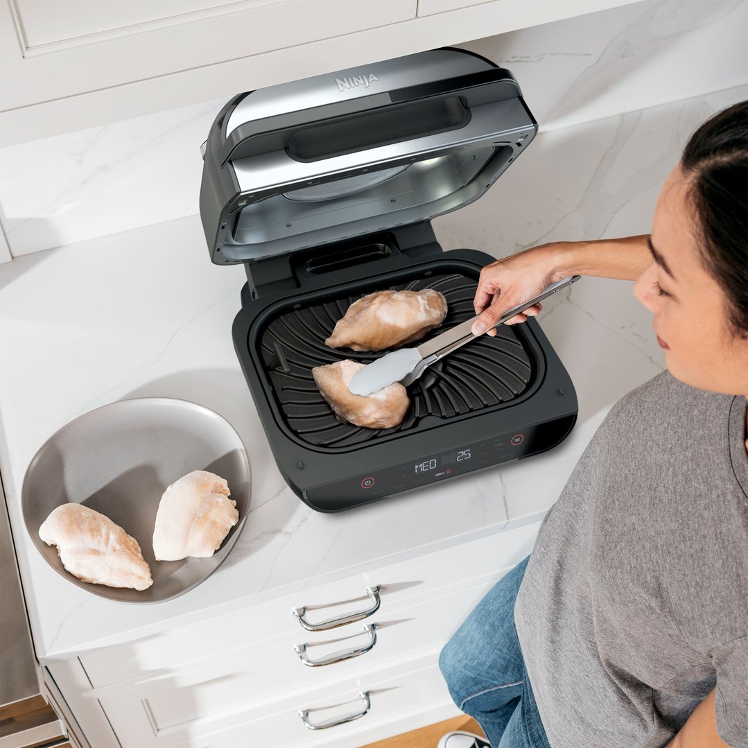 Woman using tongs to place chicken breasts into a Ninja Foodi Smart XL Grill