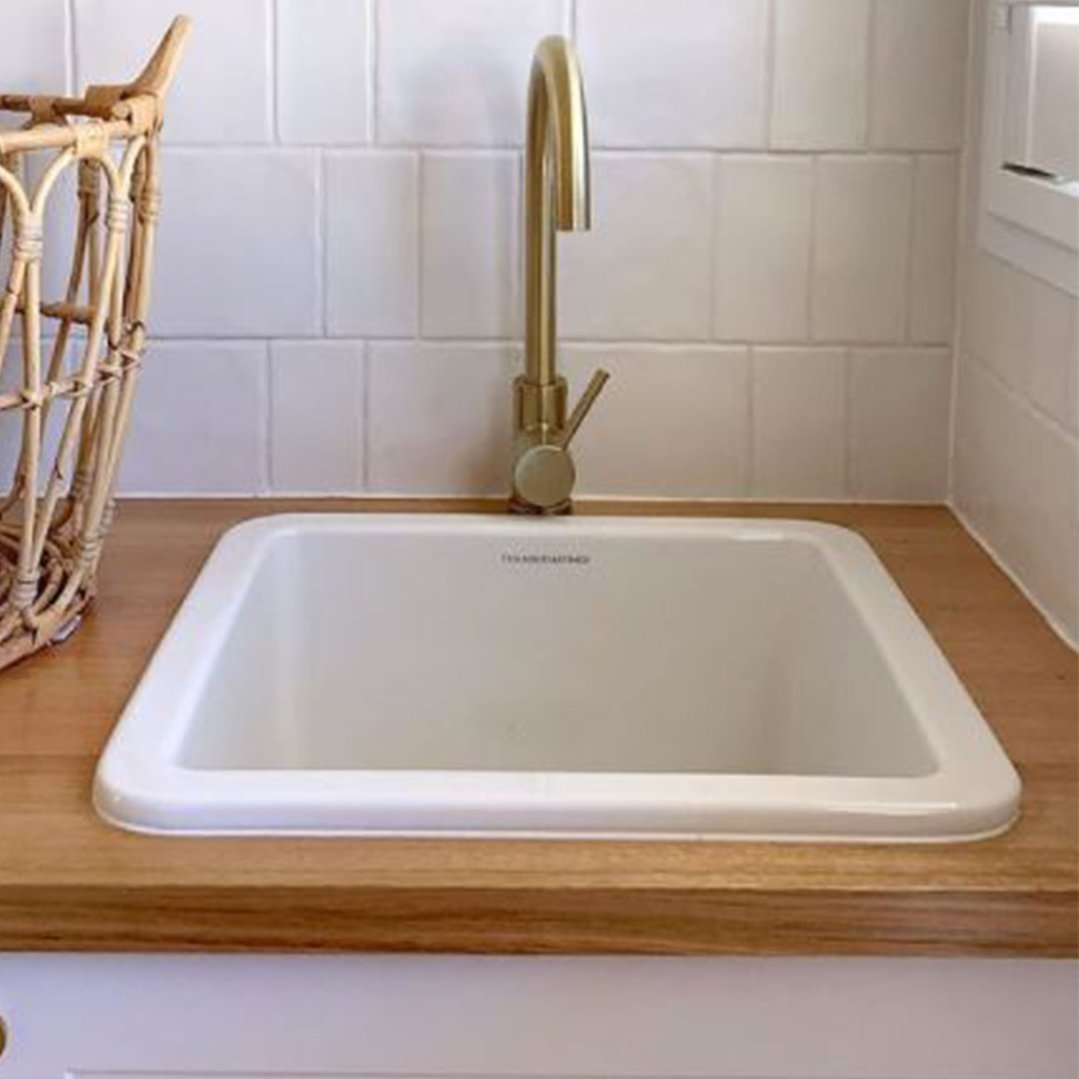 White fireclay sink with a gold faucet on a wooden countertop