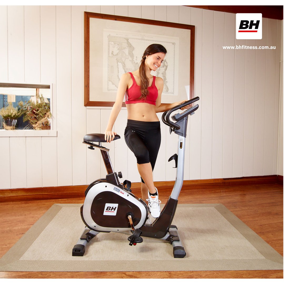 Woman standing next to a stationary bike in a room with wood paneling