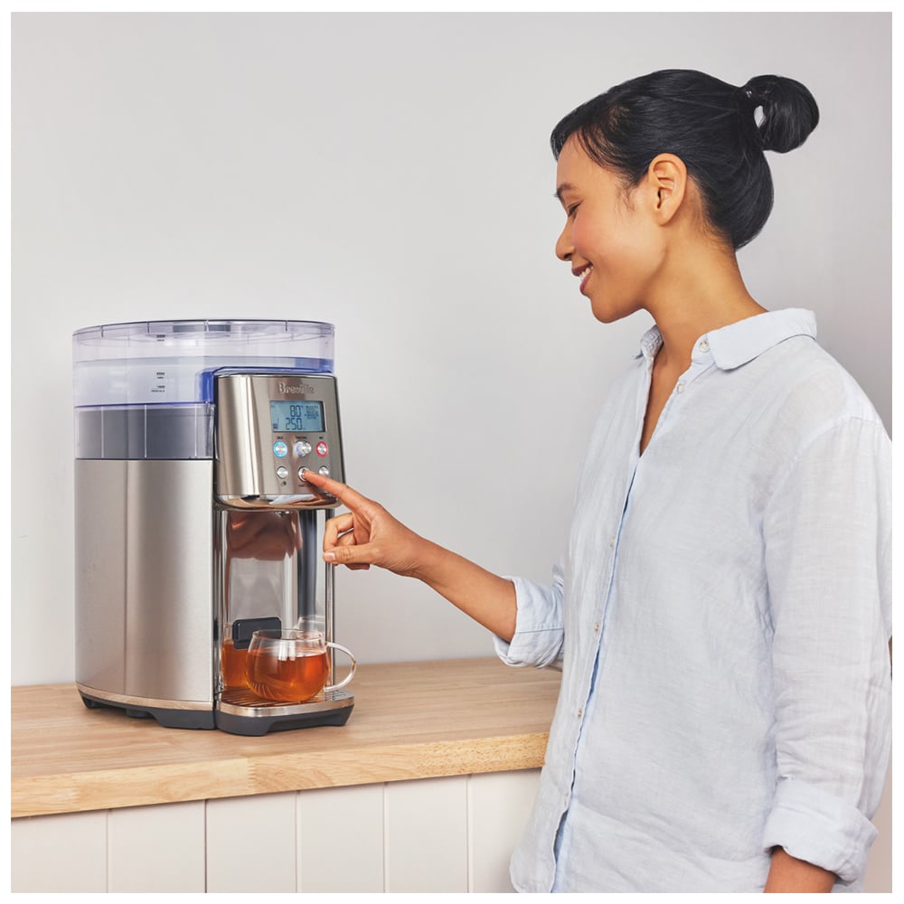Woman pressing button on a Breville AquaStation Chilled + Hot on a wooden counter