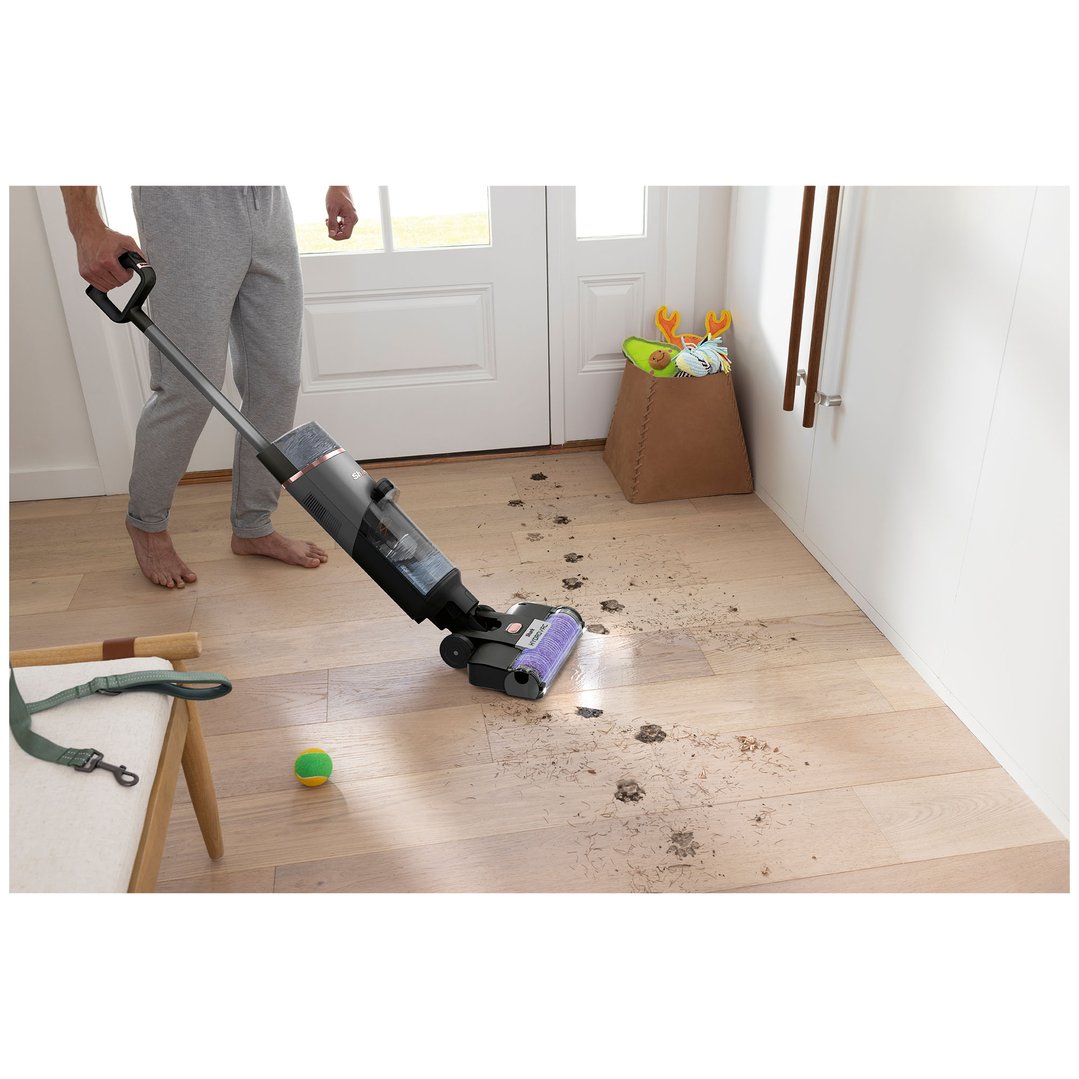 Person cleaning muddy paw prints and debris from a wooden floor with a vacuum cleaner