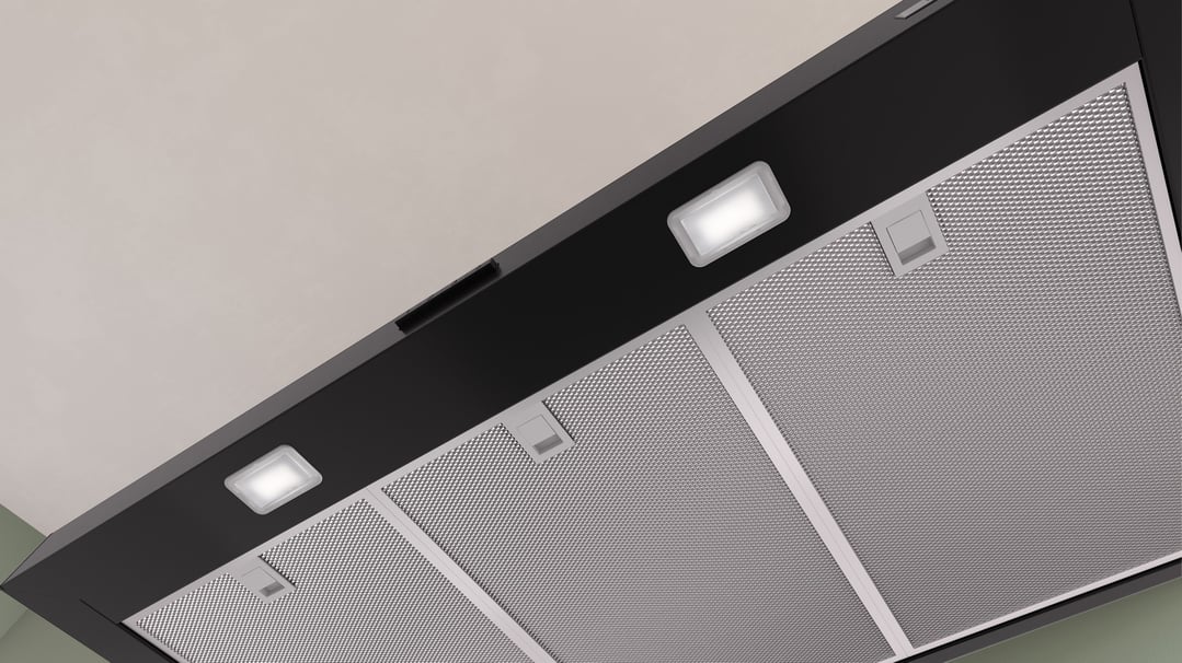 Underside of a black rangehood with lights on and metal filters visible