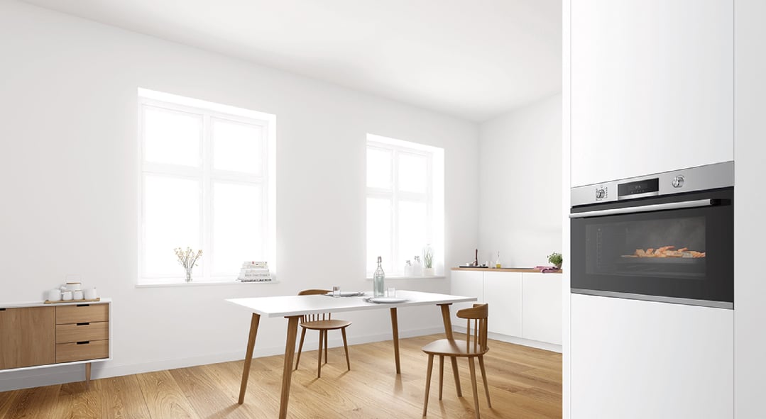 Built-in oven cooking food in a modern white kitchen with dining area