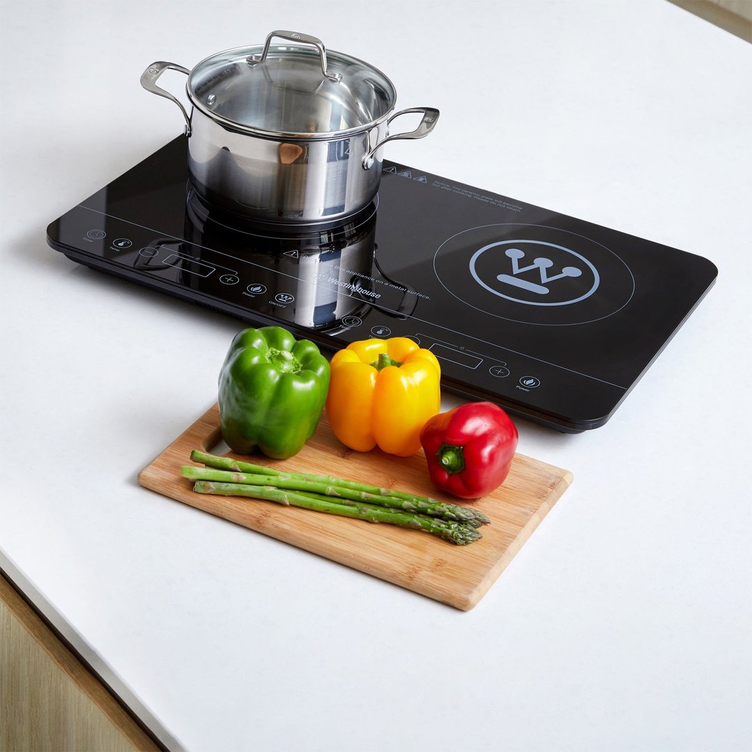 Twin induction cooktop with a pot, bell peppers, and asparagus on a white counter