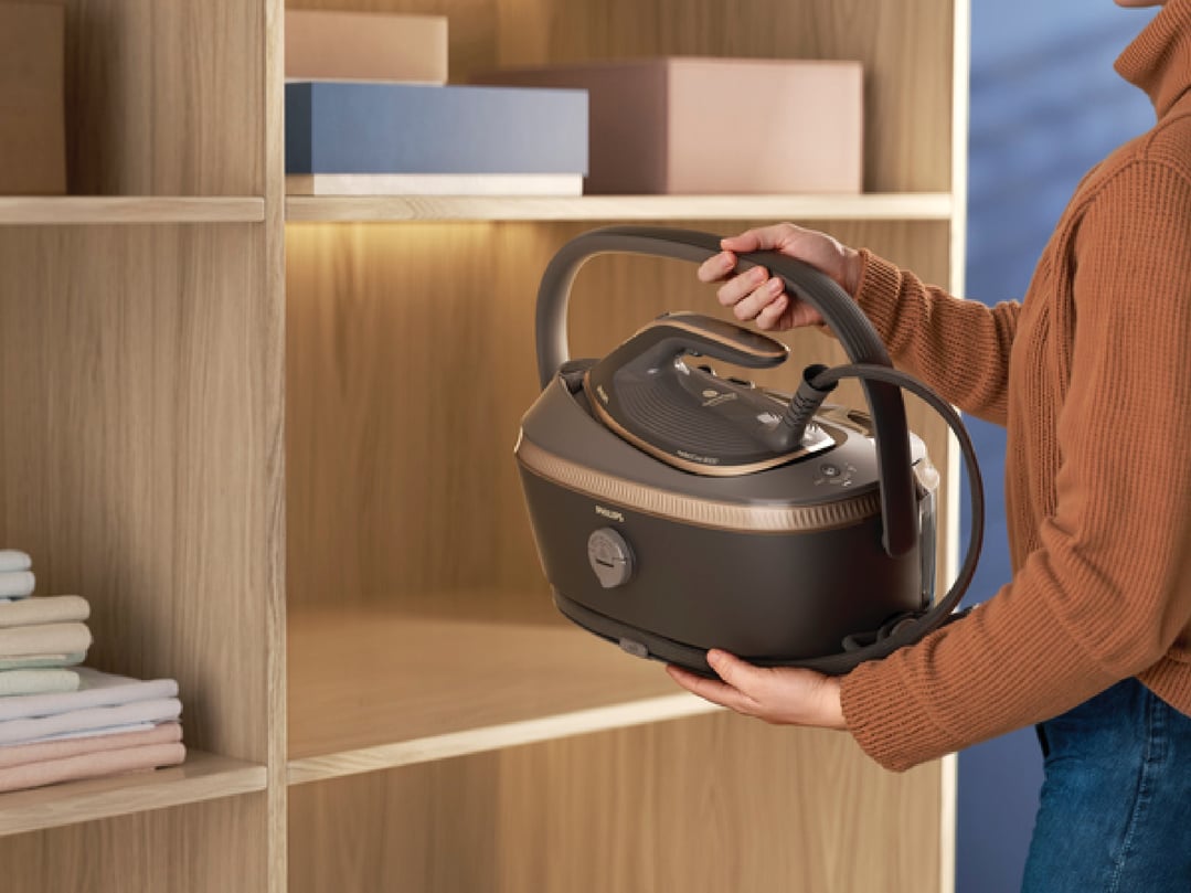 Person holding a Philips PerfectCare Steam Generator iron in a wooden cabinet