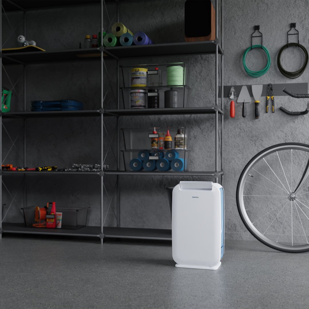 White dehumidifier on a grey floor in a garage with shelves and tools