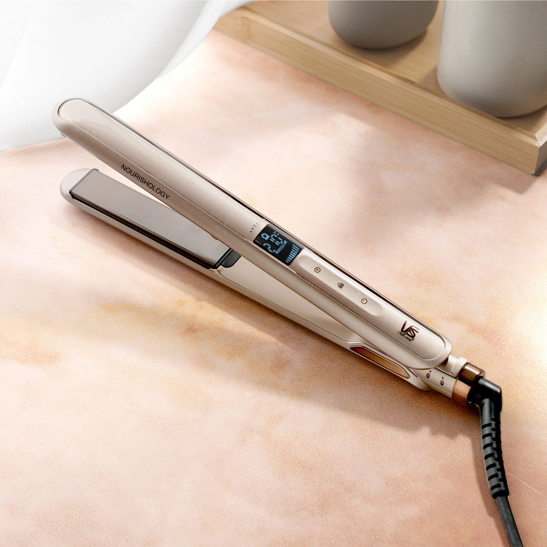 Nourishology hair straightener on a light pink surface with a wooden tray in the background