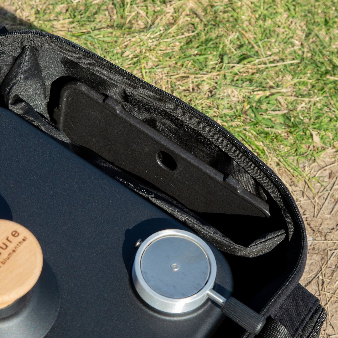 Close up of a black carrier bag with a portable barbecue on grass
