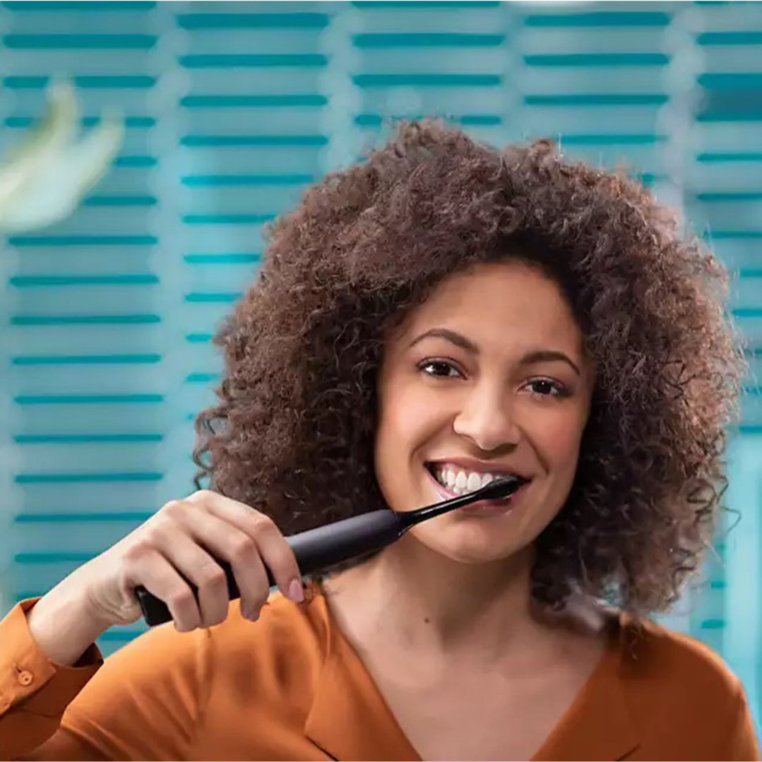 Woman brushing her teeth with a black Philips Sonicare DiamondClean 9000 electric toothbrush