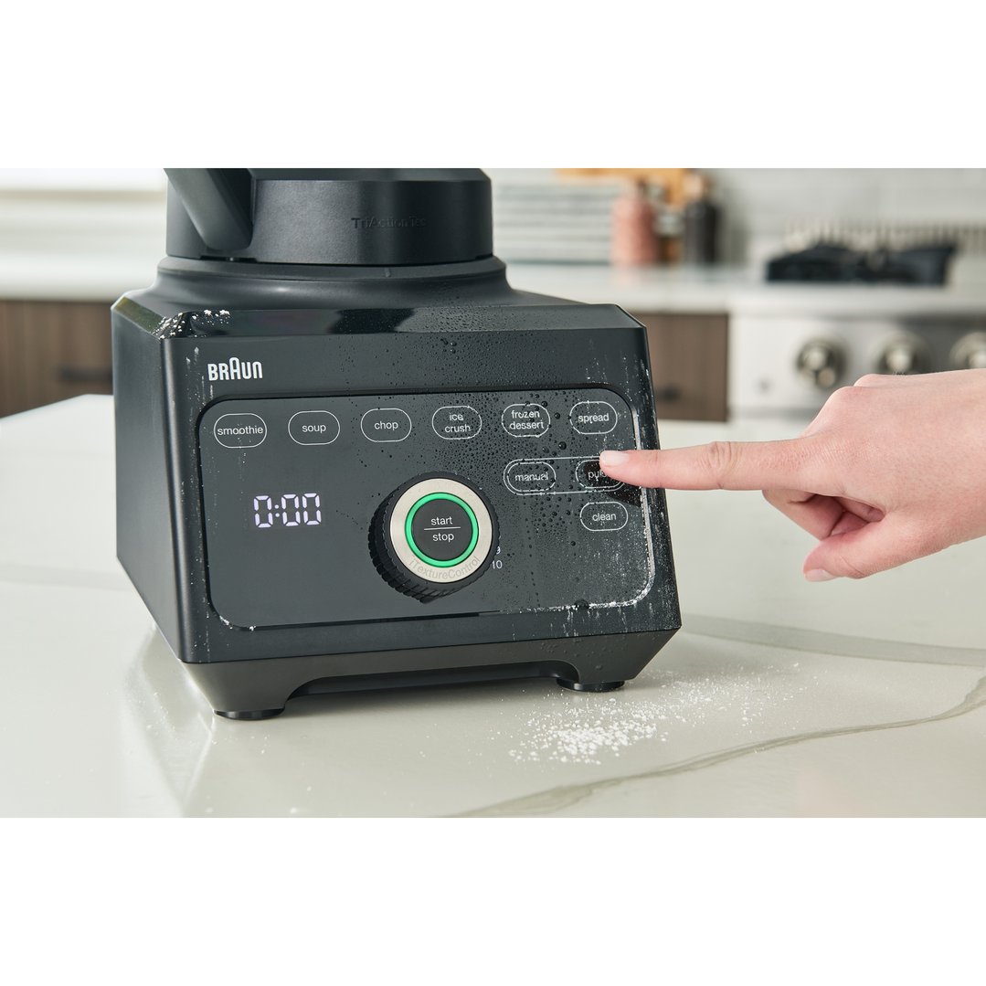 Hand pressing a button on a black Braun blender on a kitchen counter