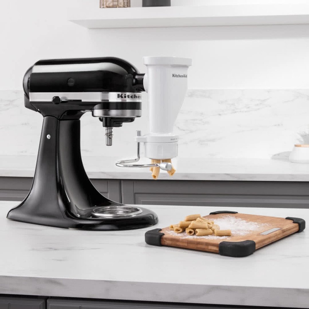 Black stand mixer with pasta press attachment making pasta on a kitchen counter