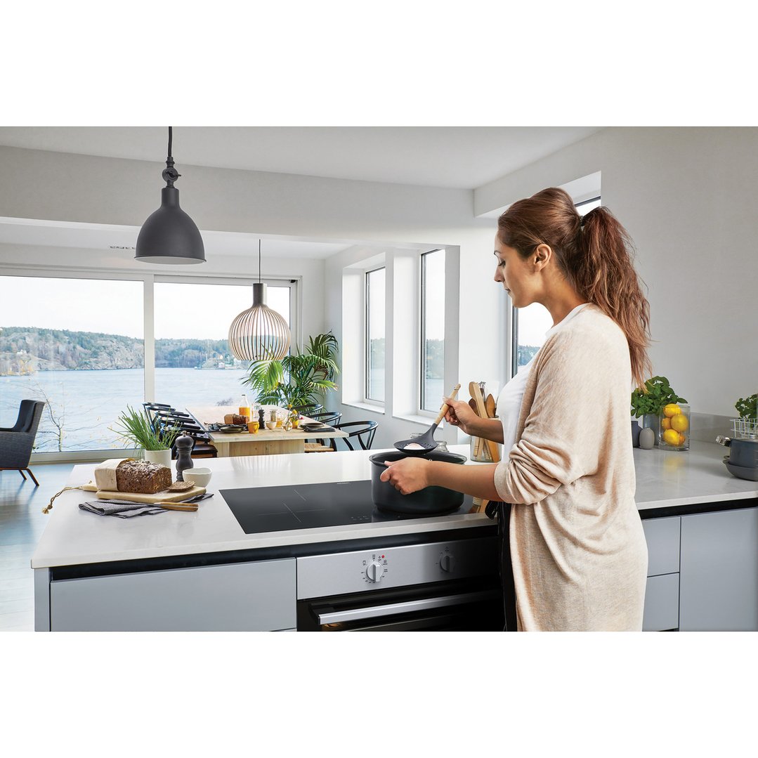 Woman cooking on a cooktop in a modern kitchen with a view of the sea