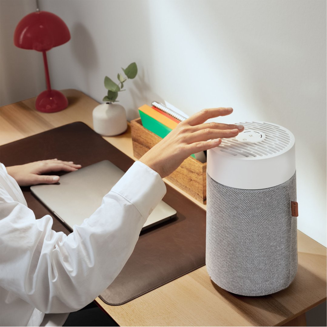 Person's hand adjusting a BLUEAIR Mini Air Purifier on a wooden desk