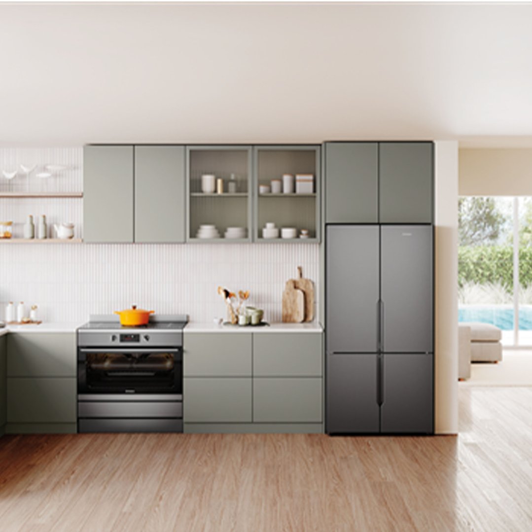 A modern kitchen with light green cabinets, a built-in oven, and a dark grey refrigerator