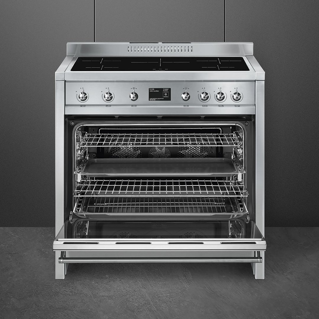 Stainless steel induction cooker with oven door open in a dark kitchen