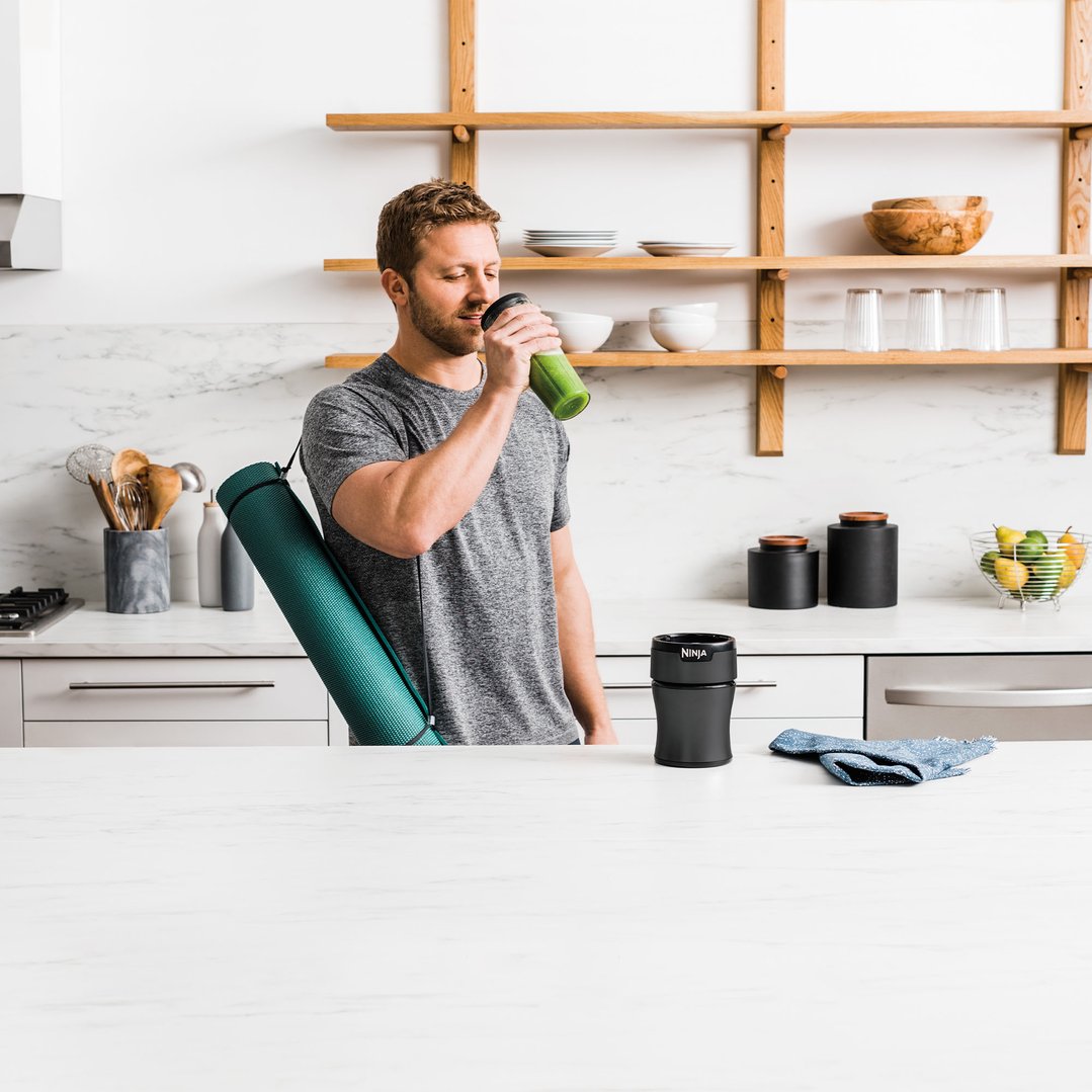 Man drinking a green smoothie from a Ninja blender cup in a kitchen