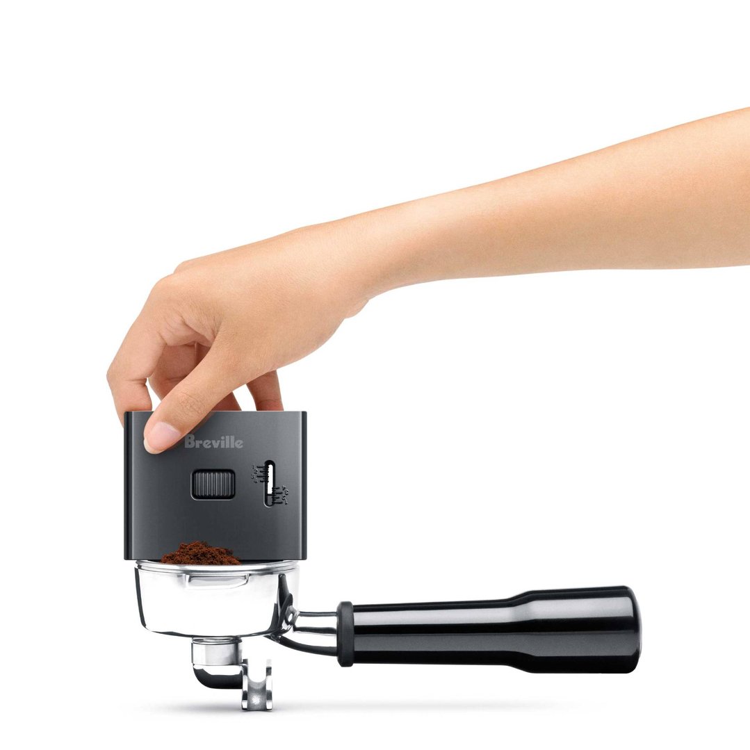Hand holding a Breville coffee grinder over a portafilter with ground coffee