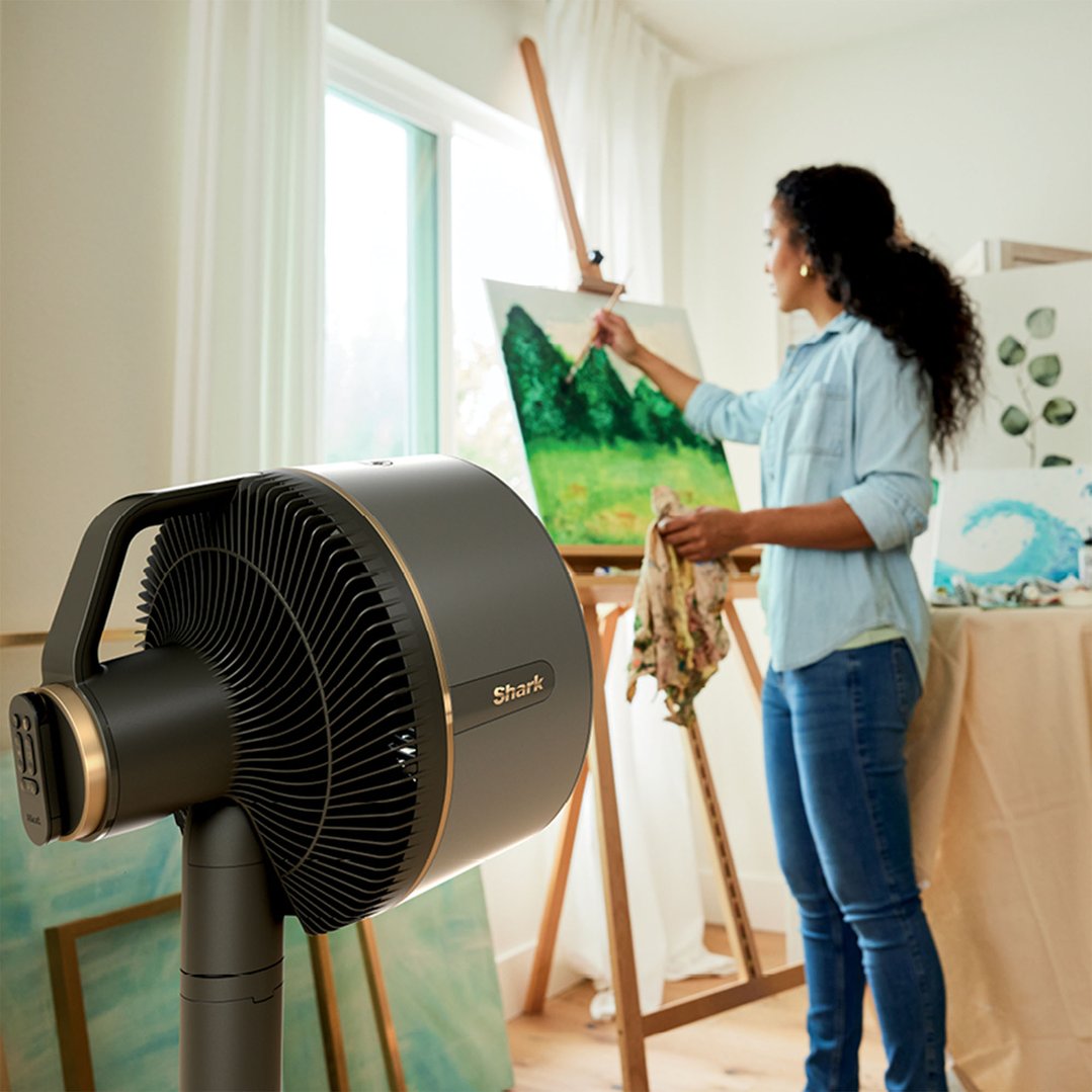 Woman painting on an easel in a bright room with a Shark FlexBreeze fan