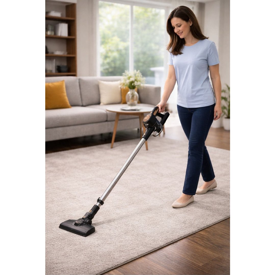 Woman vacuuming a light-colored rug in a living room with a stick vacuum
