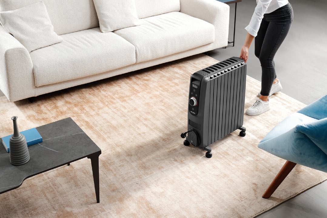 Woman moving a black oil column heater on a rug in a living room