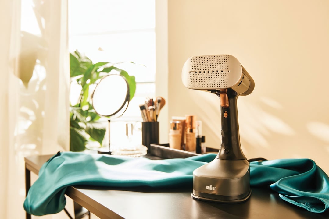 Braun Garment Steamer on a dark table with a teal garment and cosmetics