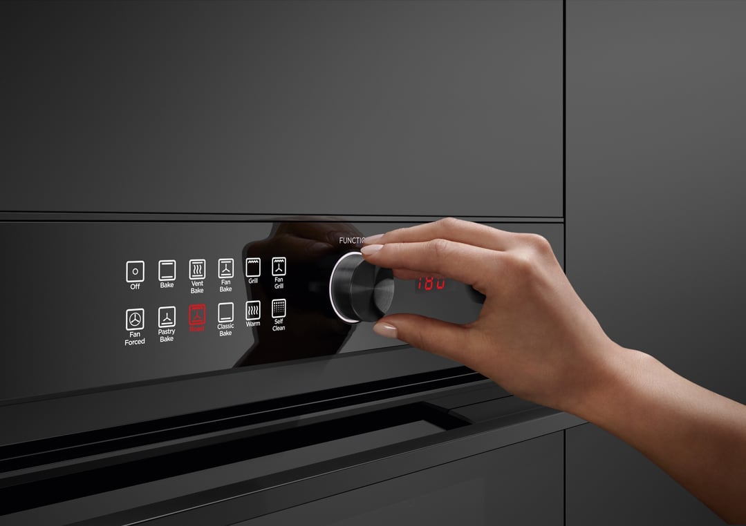 A hand adjusting the control knob on a black built-in oven
