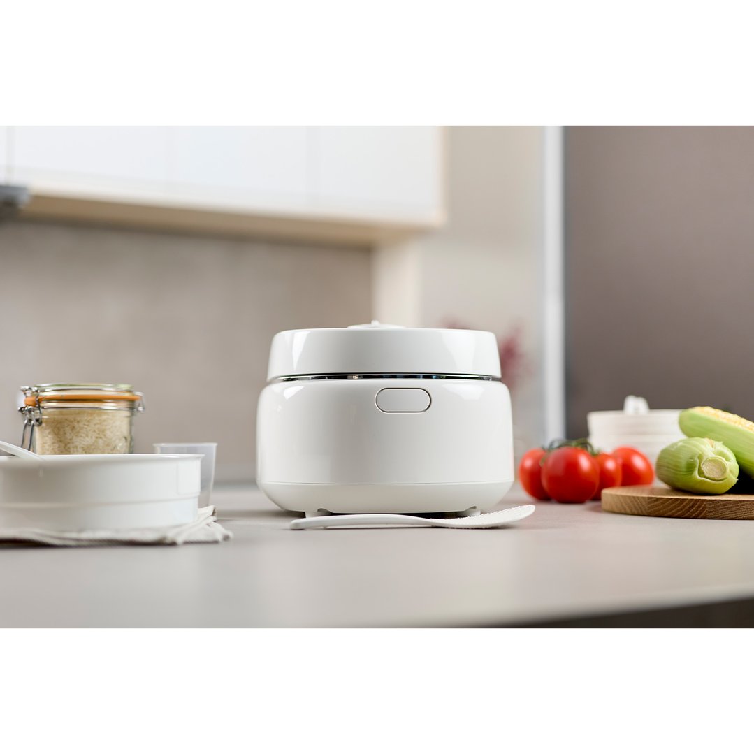 White Panasonic rice cooker on a kitchen counter with ingredients and vegetables