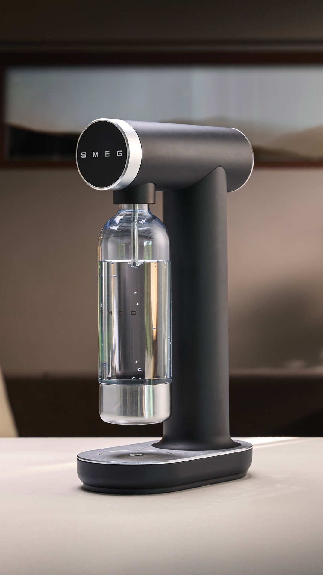 SMEG soda maker in matte black with a full bottle of water on a table