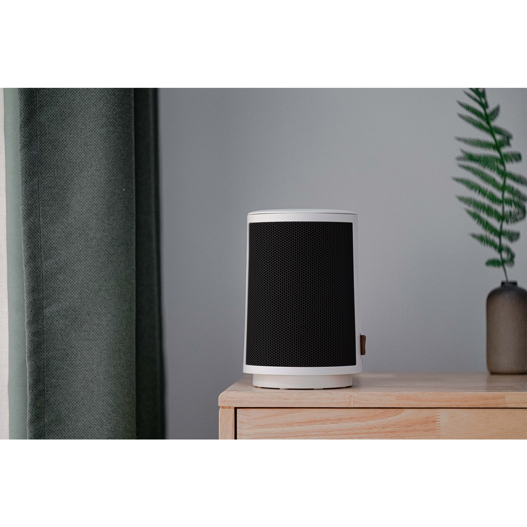 White ceramic heater on a wooden table next to a green curtain and plant