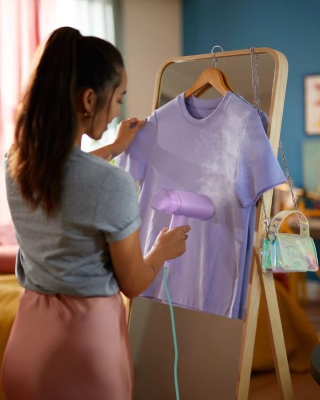 Woman using a purple handheld Garment Steamer on a purple t-shirt