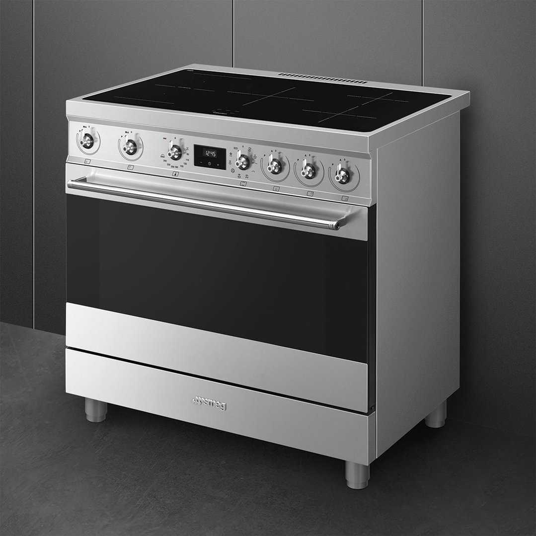 Stainless steel freestanding cooker with black cooktop and oven door in a dark room