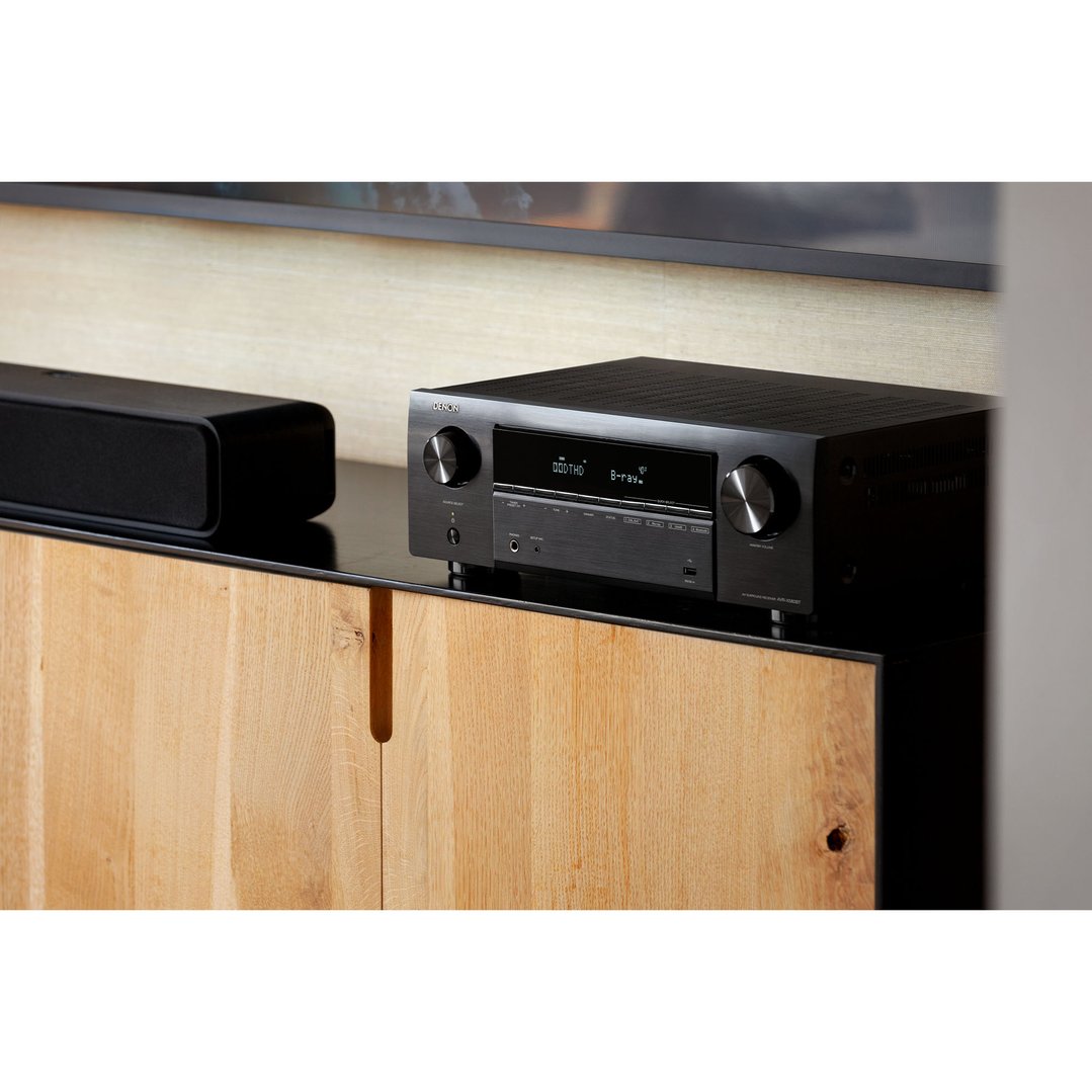 Black Denon AV receiver and soundbar on a wooden cabinet in a living room