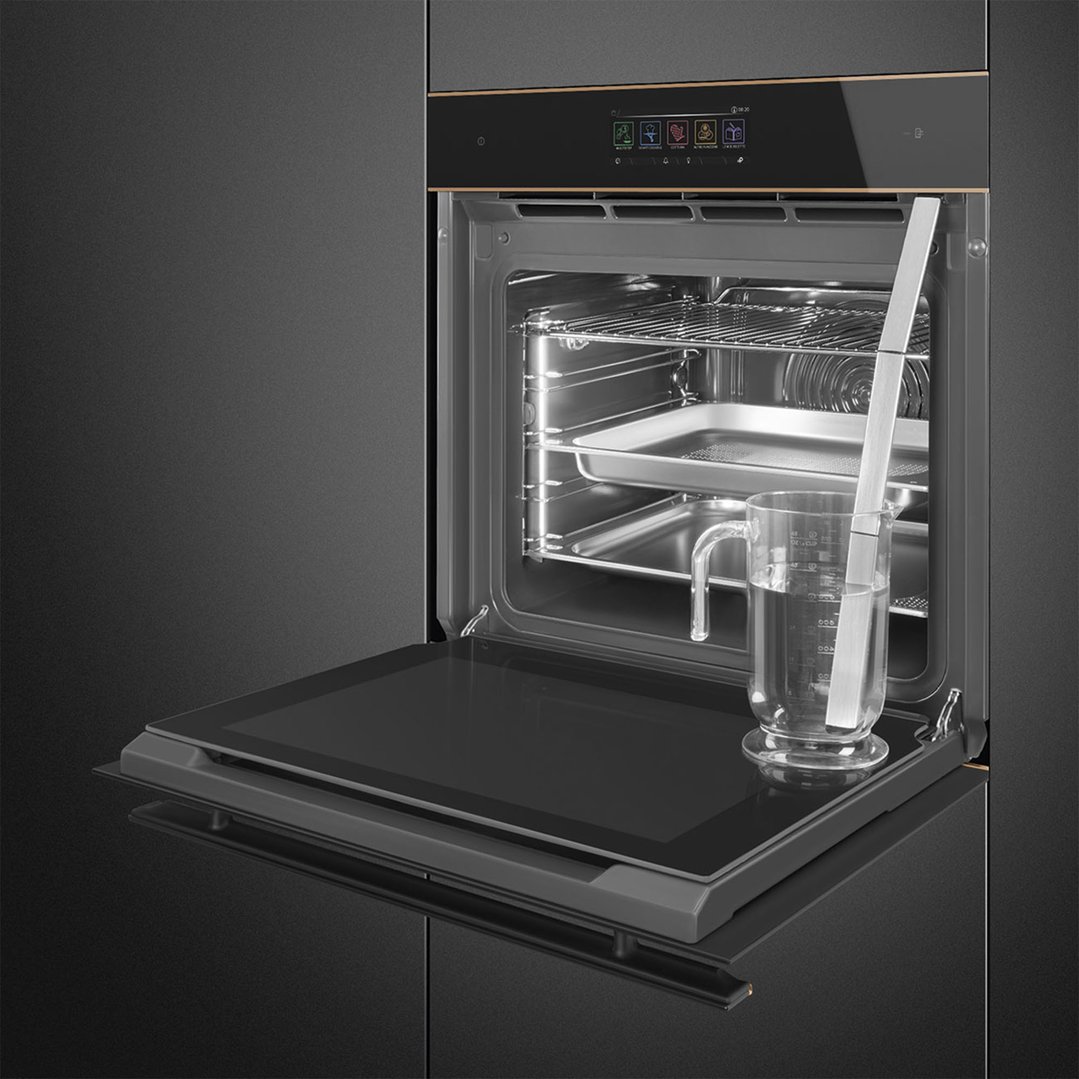 Open black glass oven with copper trim, showing interior racks and a measuring cup