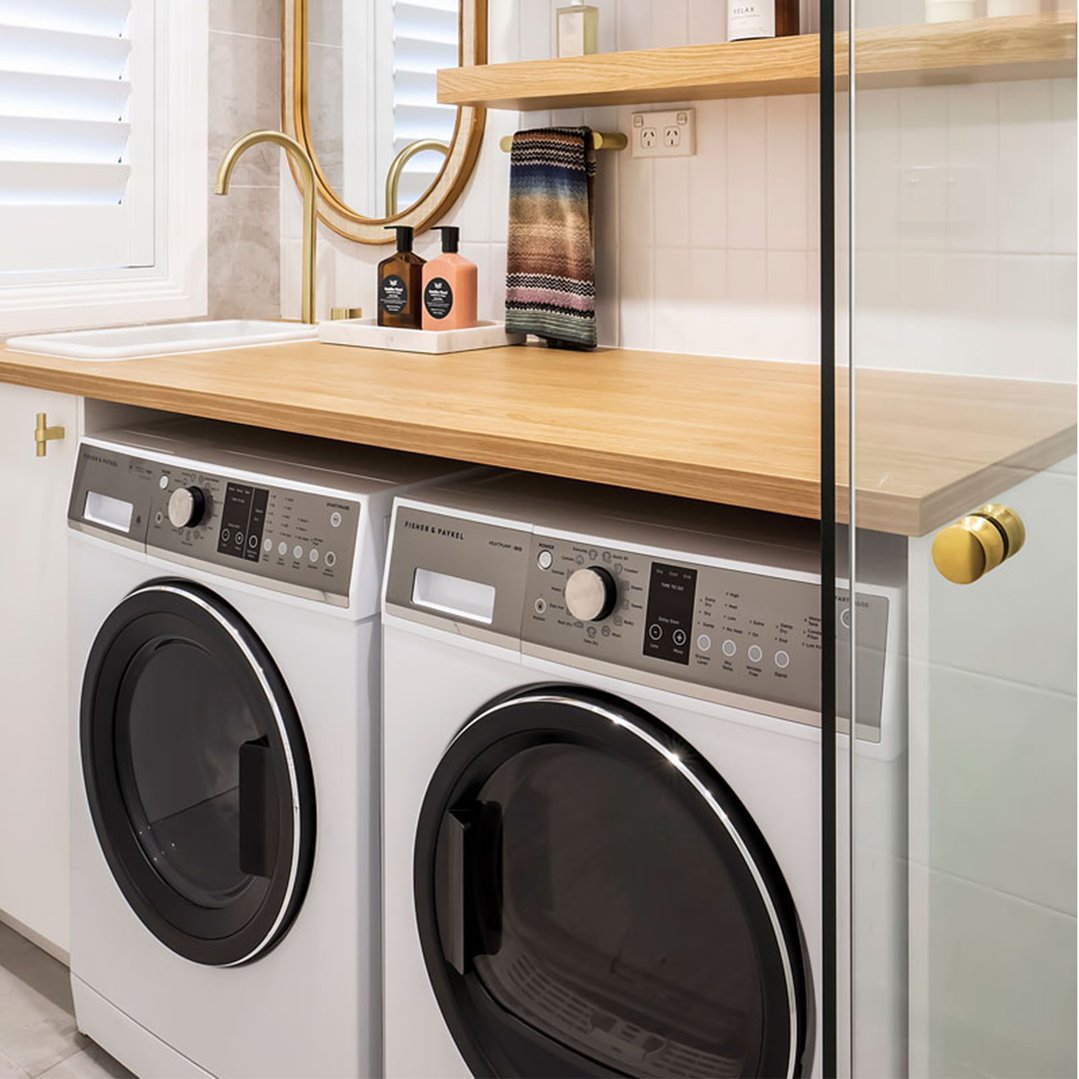 Two washing machines under a wooden countertop with a sink and faucet