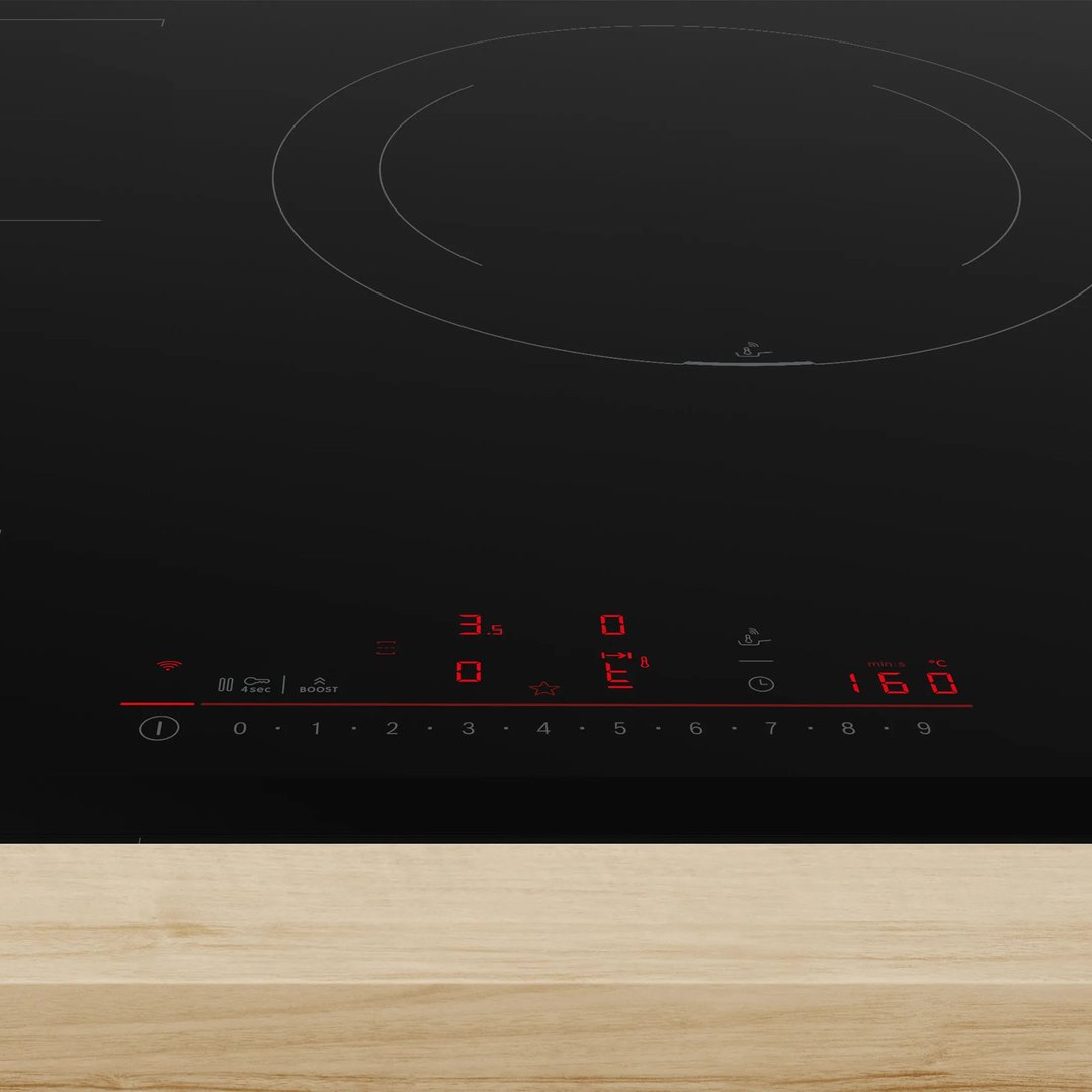 Close-up of a black induction cooktop with red digital controls on a wooden surface