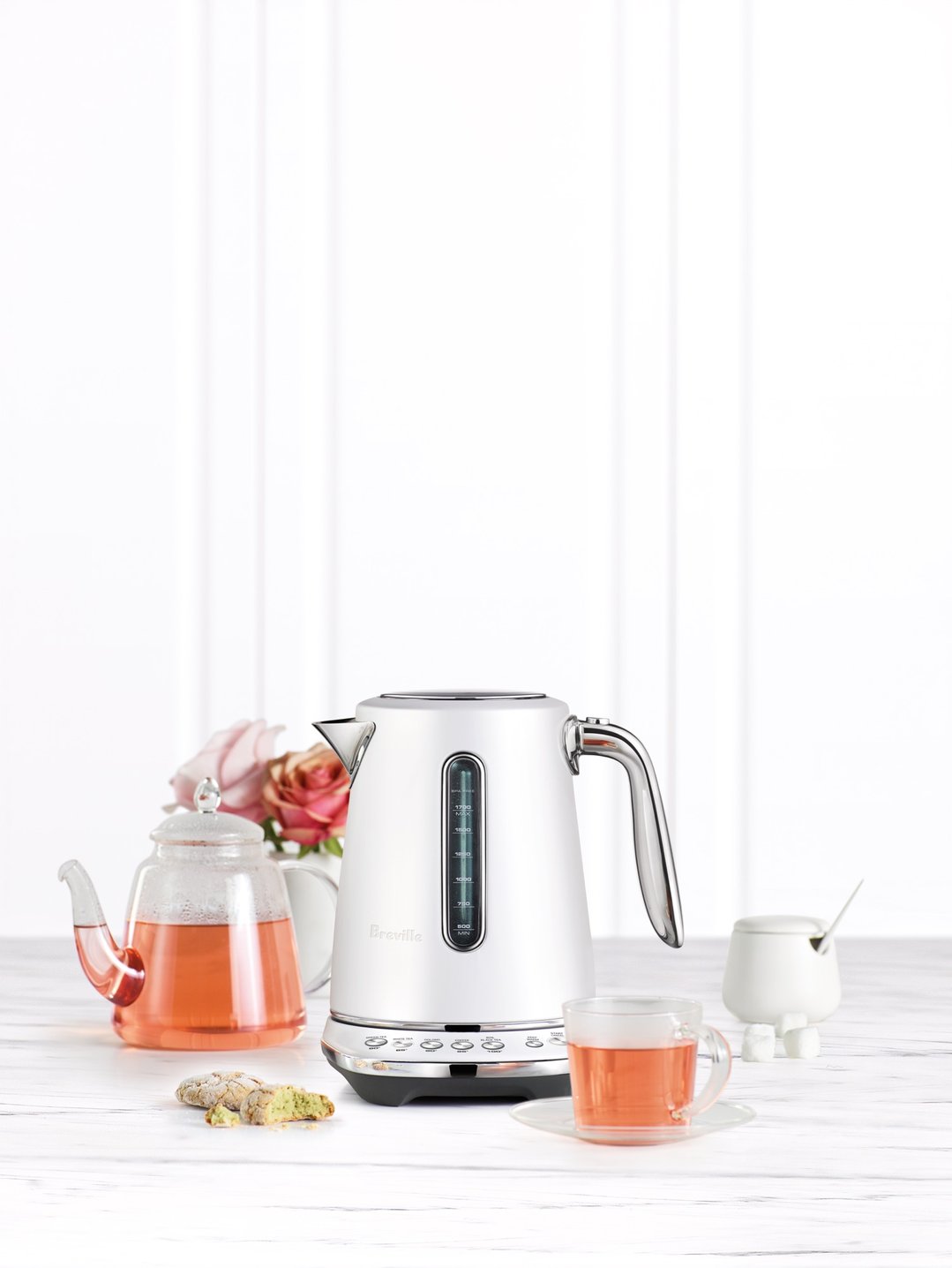 White Breville kettle on a white wooden surface with tea and cookies