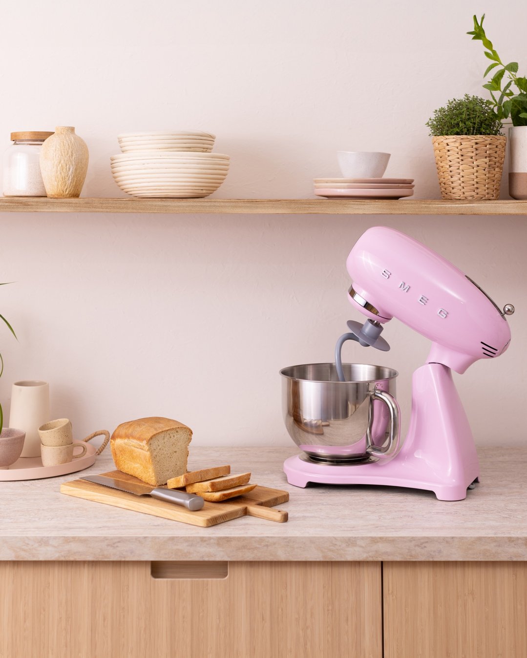 Pink Smeg stand mixer on a kitchen counter with bread and kitchenware