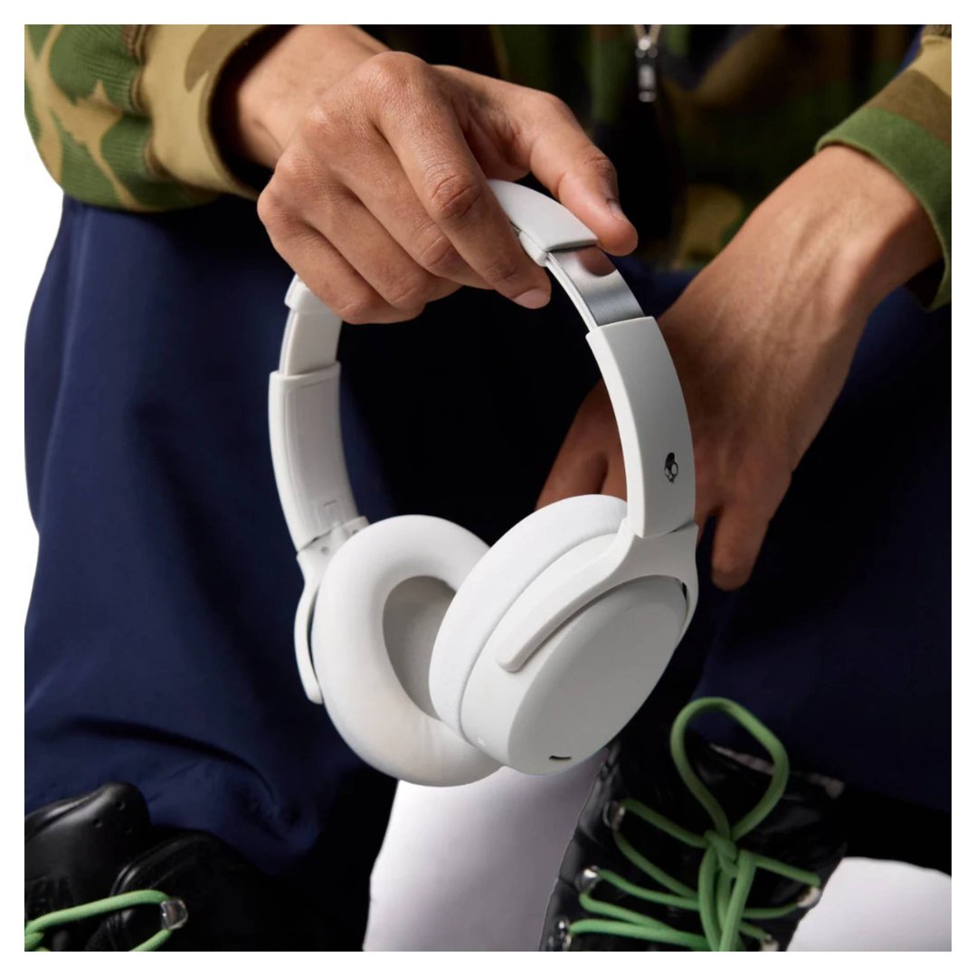 Person holding white Skullcandy Crusher ANC 2 headphones, wearing a camouflage jacket
