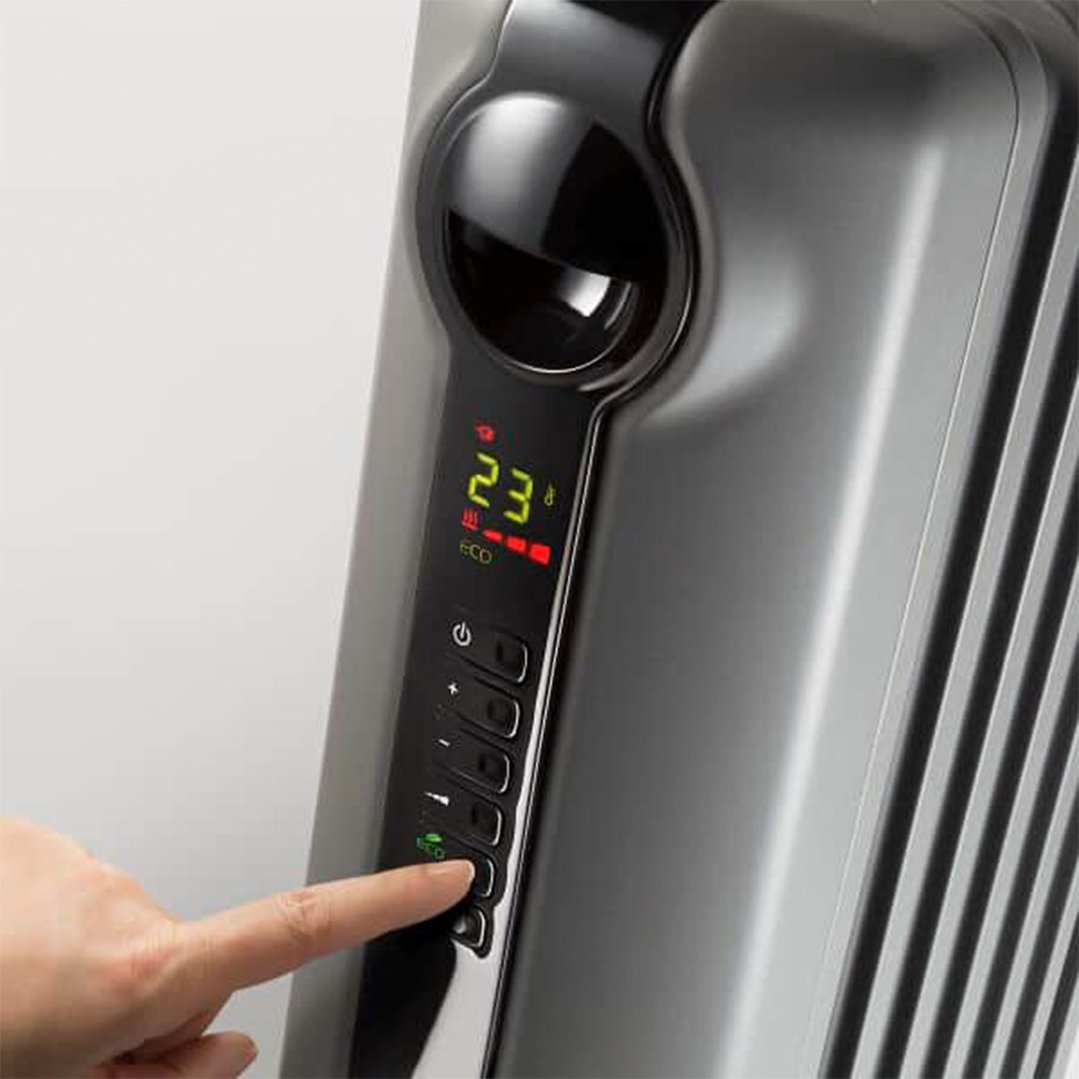 A hand pressing a button on the control panel of a grey oil column heater