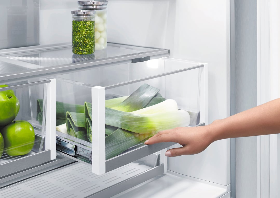 Hand pulling out a drawer of leeks in an integrated refrigerator freezer