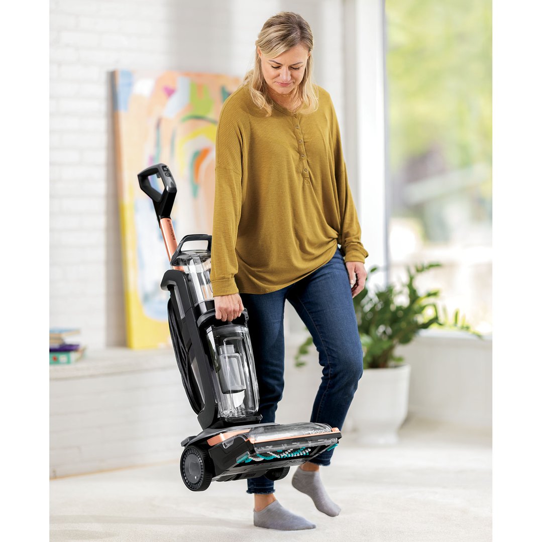 Woman in a mustard shirt and jeans carrying a BISSELL vacuum cleaner
