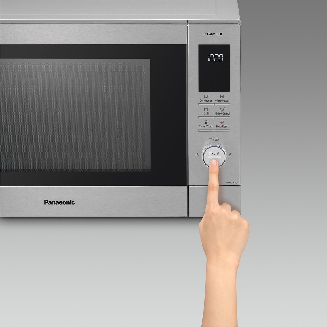 Hand pressing a button on the control panel of a Panasonic microwave oven