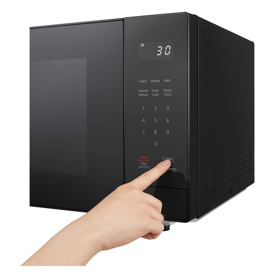 Hand pressing the start button on a black microwave control panel.
