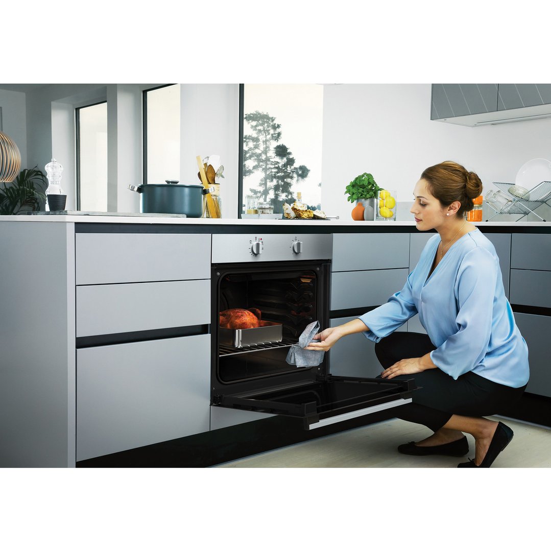 Woman checking on a roasted chicken inside a built-in oven in a modern kitchen