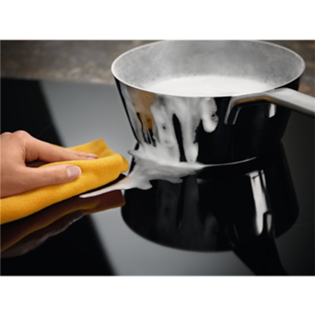 Hand wiping spilled milk from a cooktop with a yellow cloth