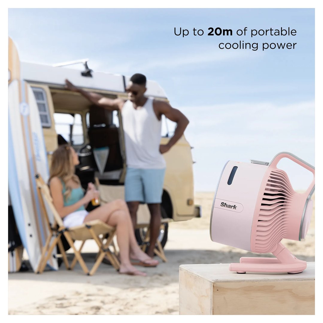 Pink portable fan on a wooden box on a beach with people and a van